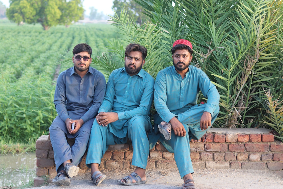 three men sitting on a brick wall in front of a field